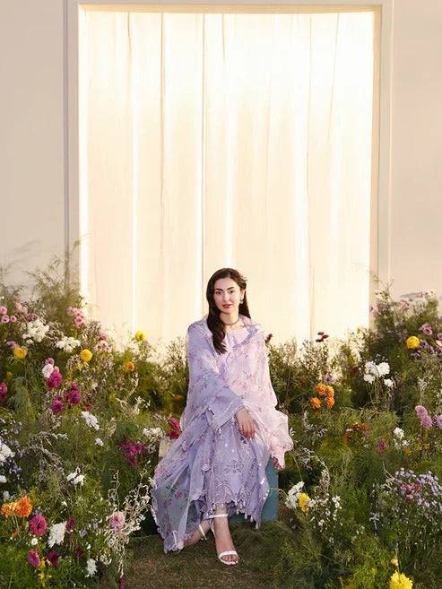 Elegant woman in lilac embroidered dress sitting among colorful flowers in front of a bright window