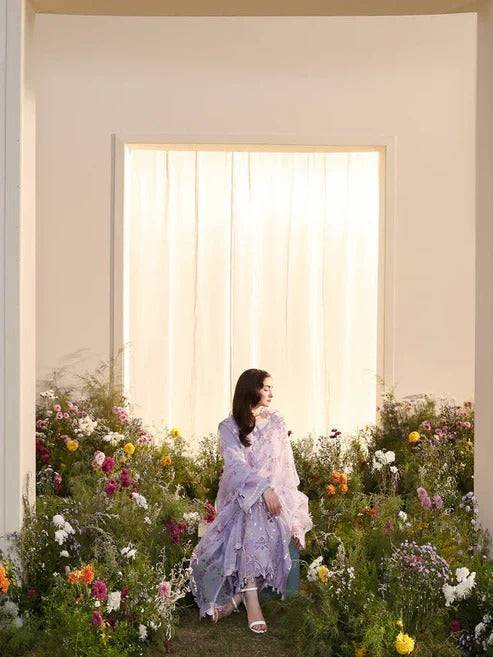 Side view of woman in lilac embroidered dress surrounded by flowers with bright window background