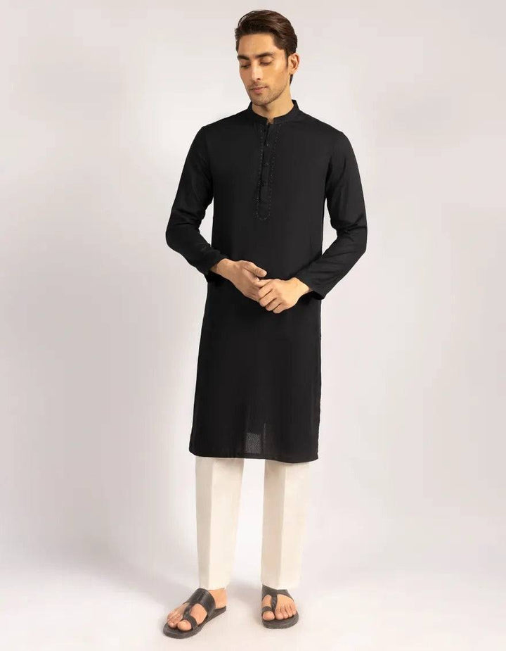 Black kurta with button placket and detailed embroidery, paired with cream trousers and sandals