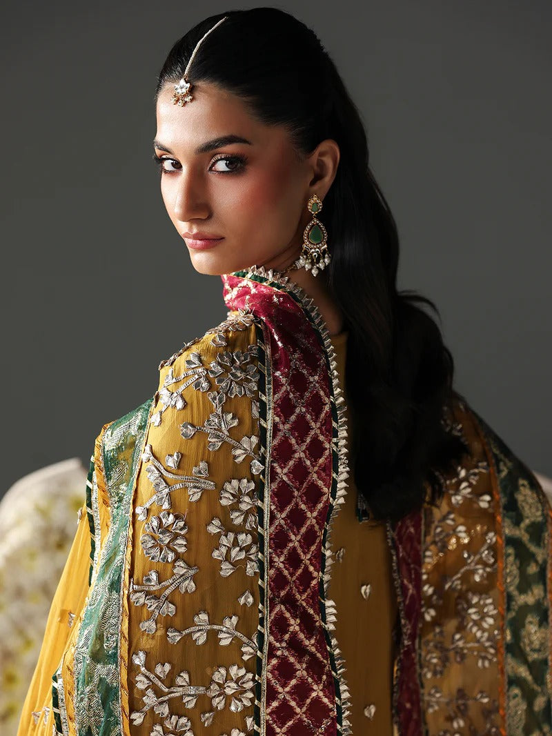 Side view of woman in yellow embroidered dress with dupatta, floral backdrop