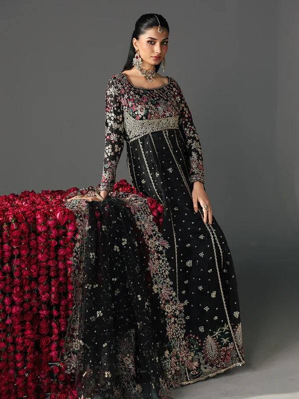 Model in black embroidered dress with floral embroidery, sitting beside red floral backdrop