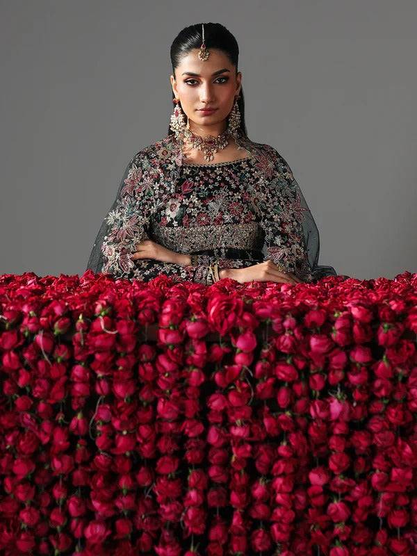 Close-up of model in black embroidered dress with floral embroidery, sitting behind red floral backdrop
