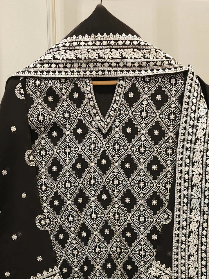 Black garment with white intricate embroidery on a hanger against a neutral background