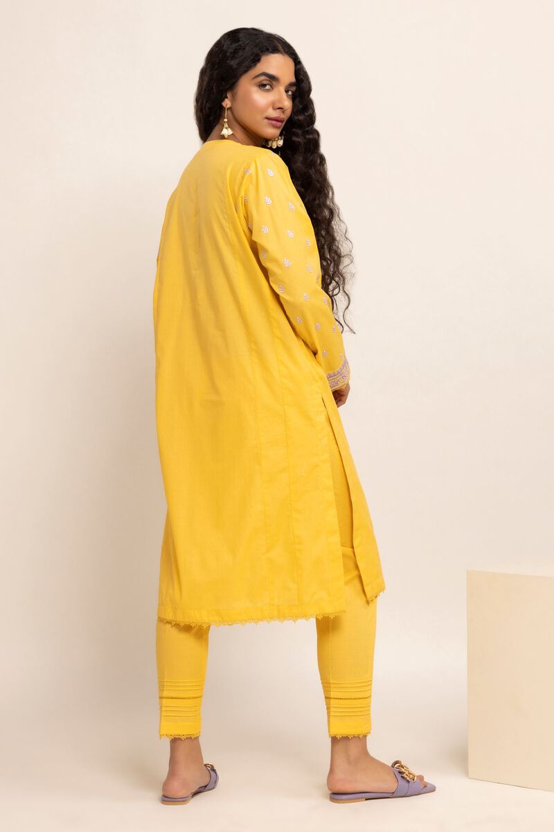 Authentic Pakistani Clothes Online a woman in a yellow outfit standing in front of a white wall