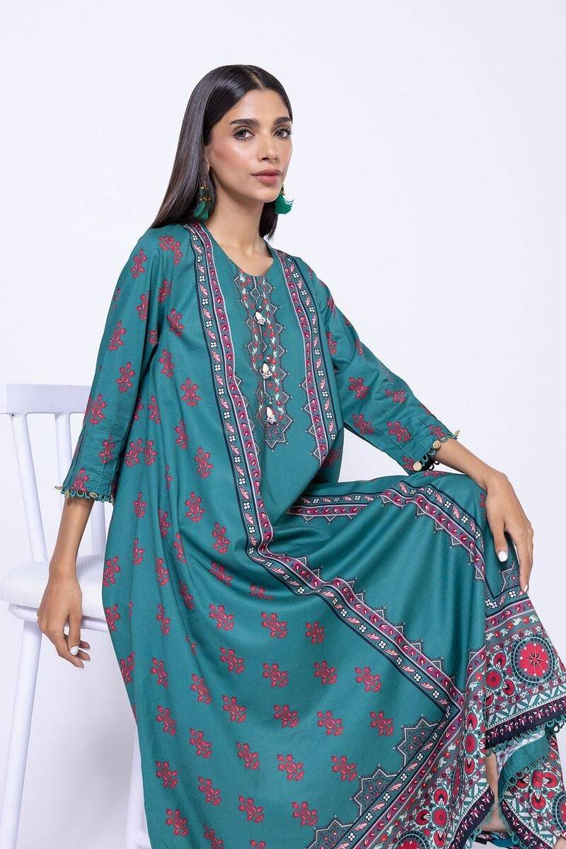 Seated model wearing teal green Khaadi kurta EET24638A with red floral patterns, asymmetrical hemline, and intricate embroidery.