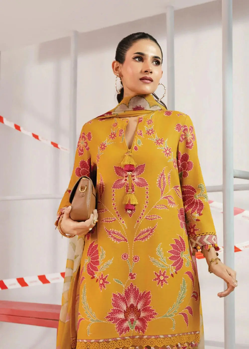 Close-up of MB-CUS25-1104-B Maria B stitched dress showing intricate pink floral embroidery on mustard khaddar shirt with tassel neckline.