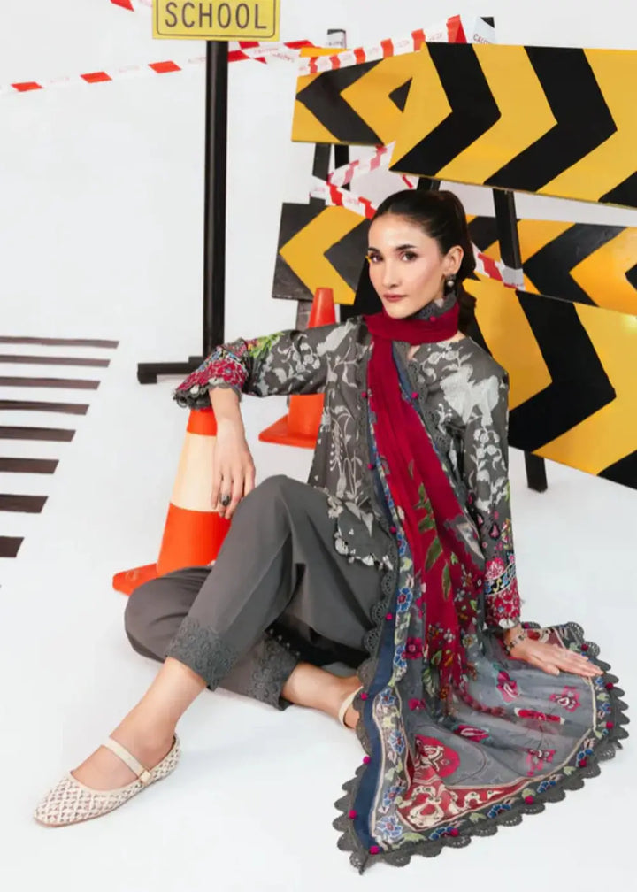 Model wearing MB-CUS25-1106-A Maria.B Stitch Suit seated with red chiffon dupatta, grey floral shirt, and embroidered linen trousers.