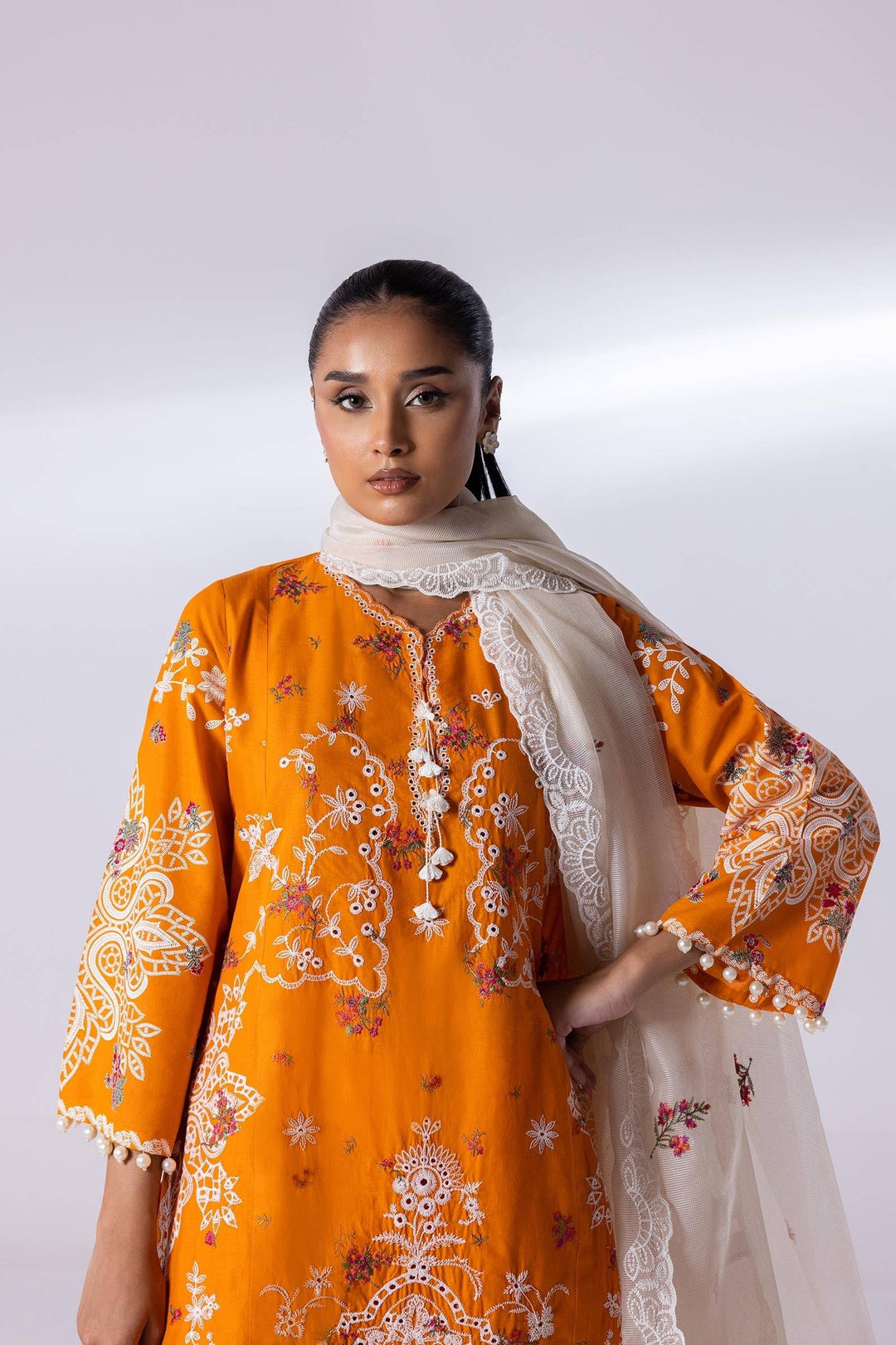 Close-up of SANA SAFINA embroidered lawn shirt in orange with white lace detailing and tassels, styled with a sheer white dupatta. Perfect for formal occasions.