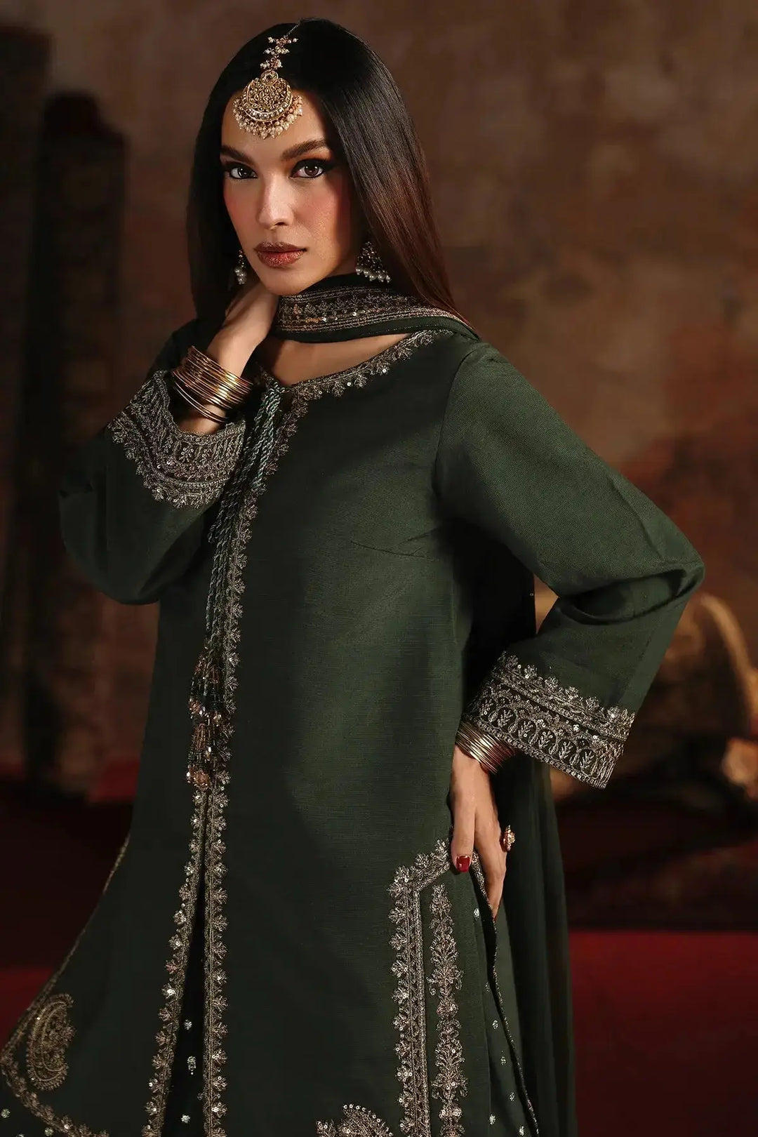 Model wearing deep emerald green embroidered raw-silk suit with silver detailing, paired with traditional jewelry, showcasing the luxurious fabric and craftsmanship